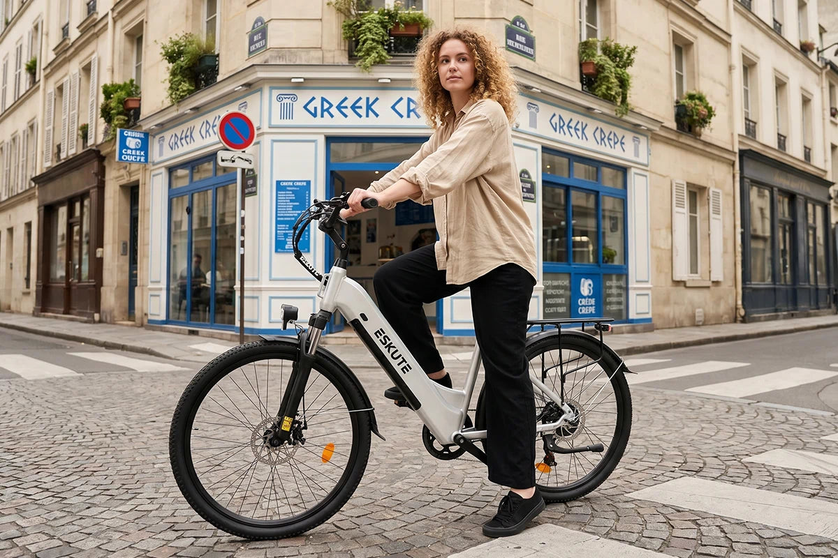 Frau fährt ein weißes C202 City-E-Bike durch eine französisch inspirierte Straße mit klassischem Café