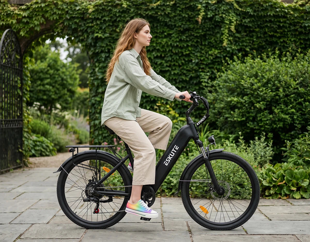 [Color:Schwarz]Frau fährt mit dem schwarzen Eskute C202 City-E-Bike ruhig entlang eines grünen Gartens.