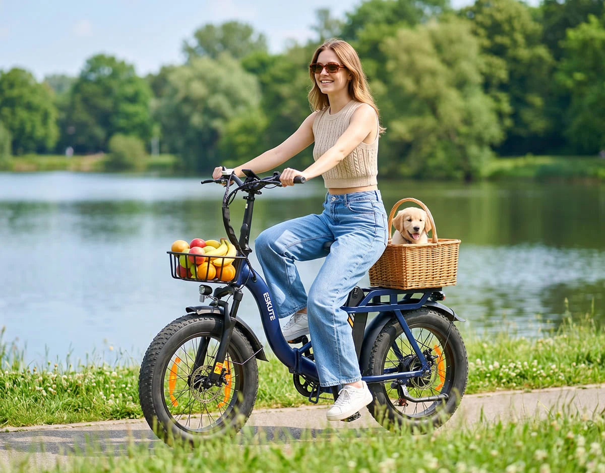 [Color:Blau]Eskute D202 Klapp-E-Bike fährt auf einem Parkweg am See mit Einkaufskorb und Haustiertransport